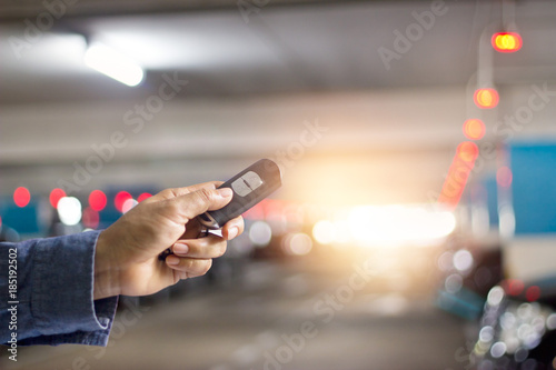 Hand with a key remote control of car on underground parking background