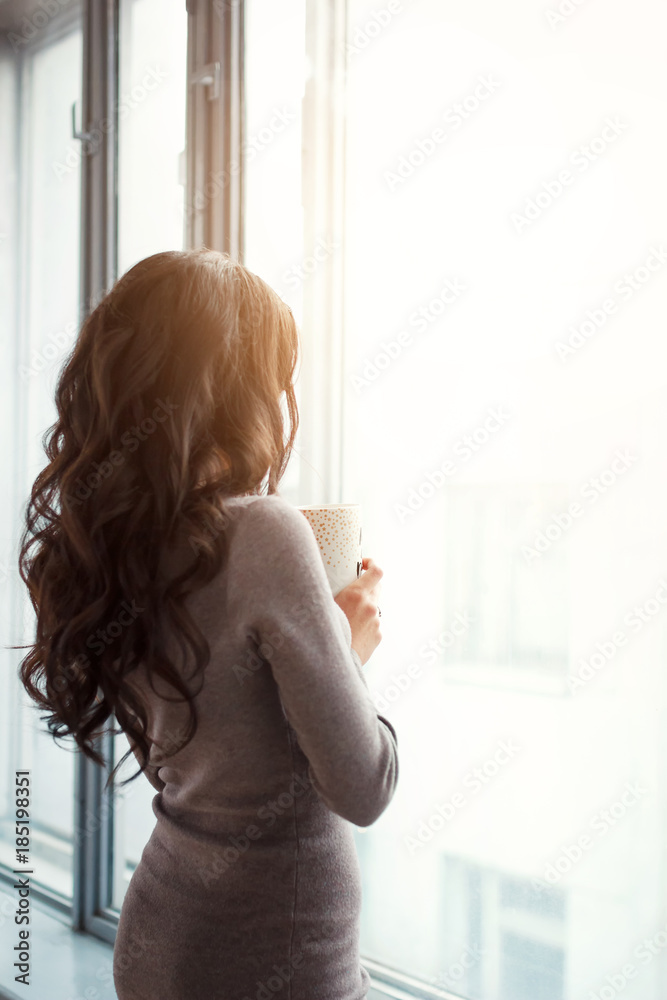beautiful slender girl by the window with a cup of coffee in her beautiful slender girl by the window with a cup of coffee in her