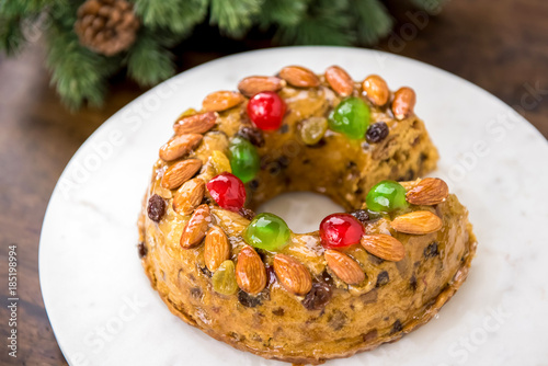 Colorful Christmas fruitcake topped with almonds and glace cherries on white platter