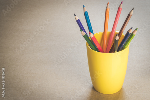 A lots of colour pencils in yellow cup on wooden texture paper.