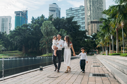 happy stylish parents holding hands with son and daughter walking in sunny street, amazing family moment. father's mother's day