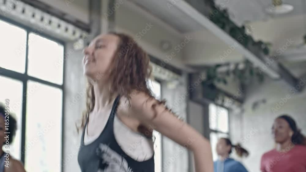 Medium shot with low angle of curly young woman jumping and doing aerobics in group class Medium shot with low angle of curly young woman jumping and doing aerobics in group class