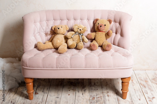 Three teddy bears sitting on pink sofa. photo