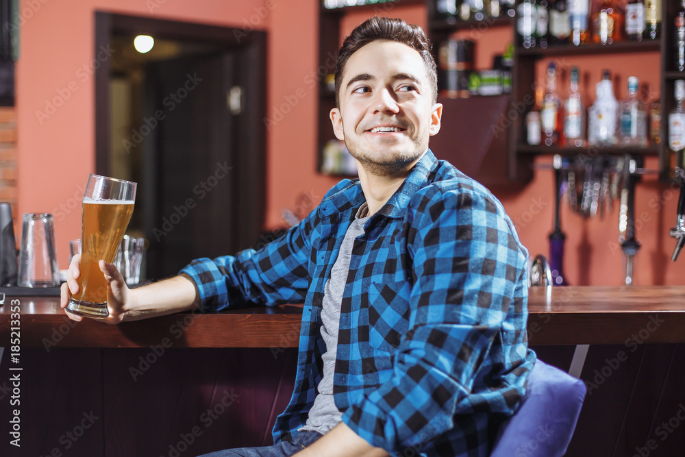 Young handsome smiling man drinking beer and watching the game on TV in the bar Young handsome smiling man drinking beer and watching the game on TV in the bar