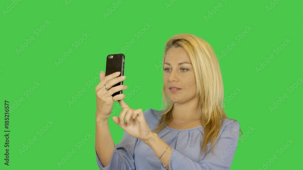 Blonde young woman is taking photo self portrait on a smartphone transparent green screen background. Alpha channel. Blonde young woman is taking photo self portrait on a smartphone transparent green screen background. Alpha channel.