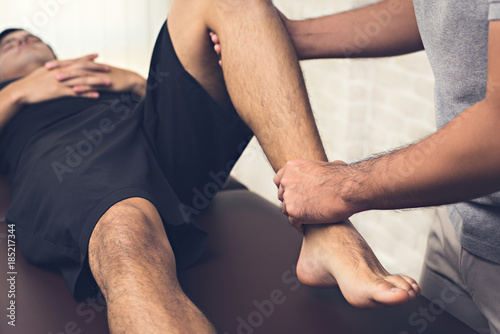 Therapist treating injured leg of athlete male patient in clinic