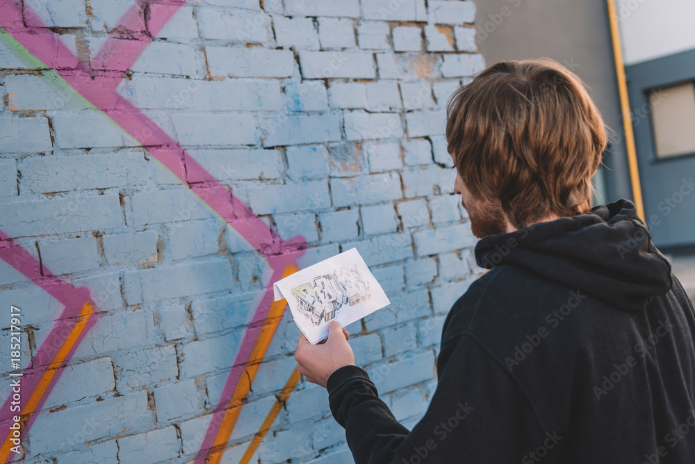 street artist looking at sketch and painting colorful graffiti on wall