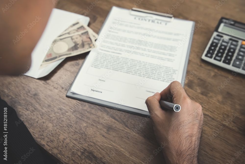 Obraz premium Hand holding pen signing contract with money, Japanese yen currency, on the table