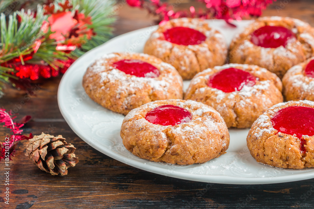 Fototapeta premium Traditional German Christmas cookies Engelsaugen with red berry jam on a white plate on the wooden table