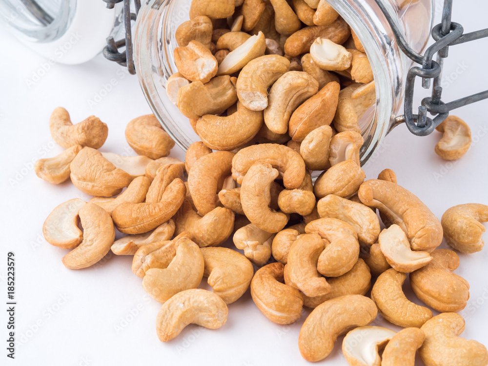 Fototapeta premium Glass bottle with cashew nuts on white background. A glass bowl with a scattering of nuts, side view,
