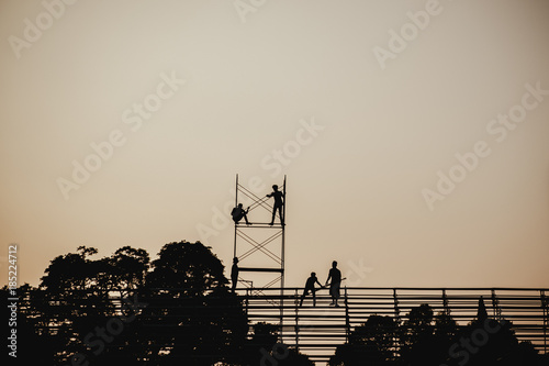 Silhouette image of a group of workers working on scaffolding for construction in the evening