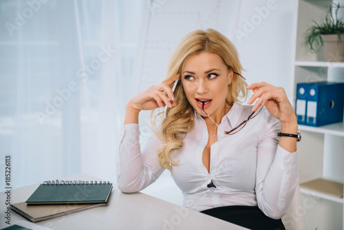 attractive sexy businesswoman talking by smartphone in office and biting glasses © LIGHTFIELD STUDIOS