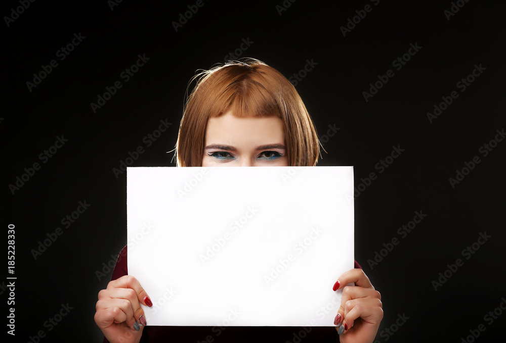 Red-haired woman holding an empty A4 card. Isolated on black background. Space for text Red-haired woman holding an empty A4 card. Isolated on black background. Space for text