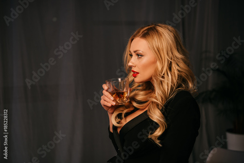 side view of attractive sexy blonde woman drinking whiskey in office at evening