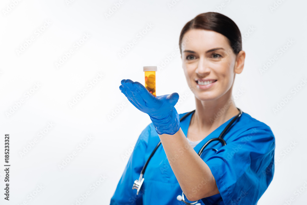 Test of medication. Attractive positive female laboratorian placing medication at palm and smiling while posing on the isolated background Test of medication. Attractive positive female laboratorian placing medication at palm and smiling while posing on the isolated background