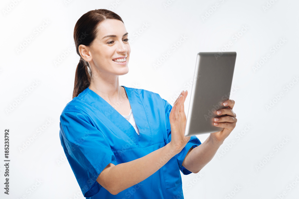 Technology helps.  Energetic budding female doctor swiping photo at tablet while standing on white background and grinning