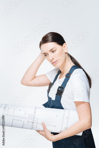 Hard work. Vigorous positive female architect  examining  plan while carrying blueprint  and staring down photo