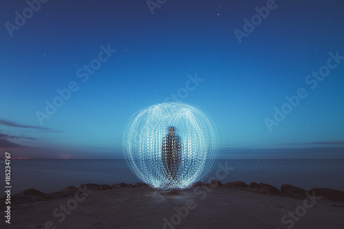 Person creating light ball at seashore at night 
