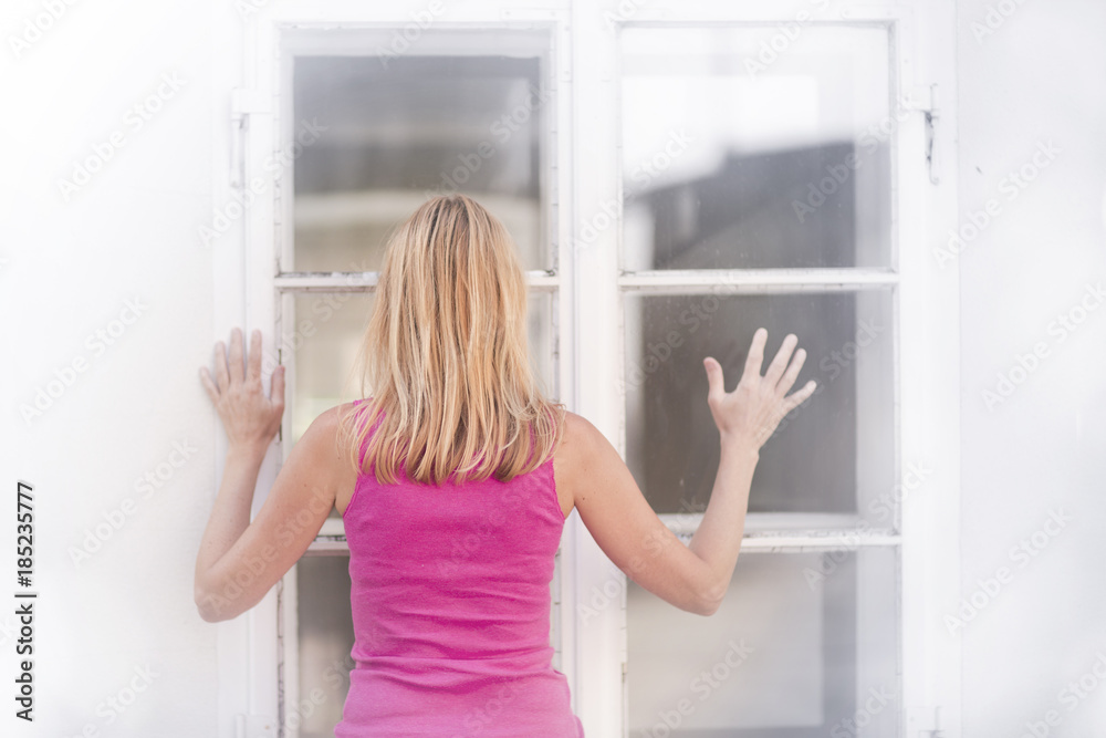Sad woman stands in front of a closed window