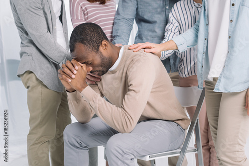 cropped shot of people supporting depressed middle aged african american man during group therapy