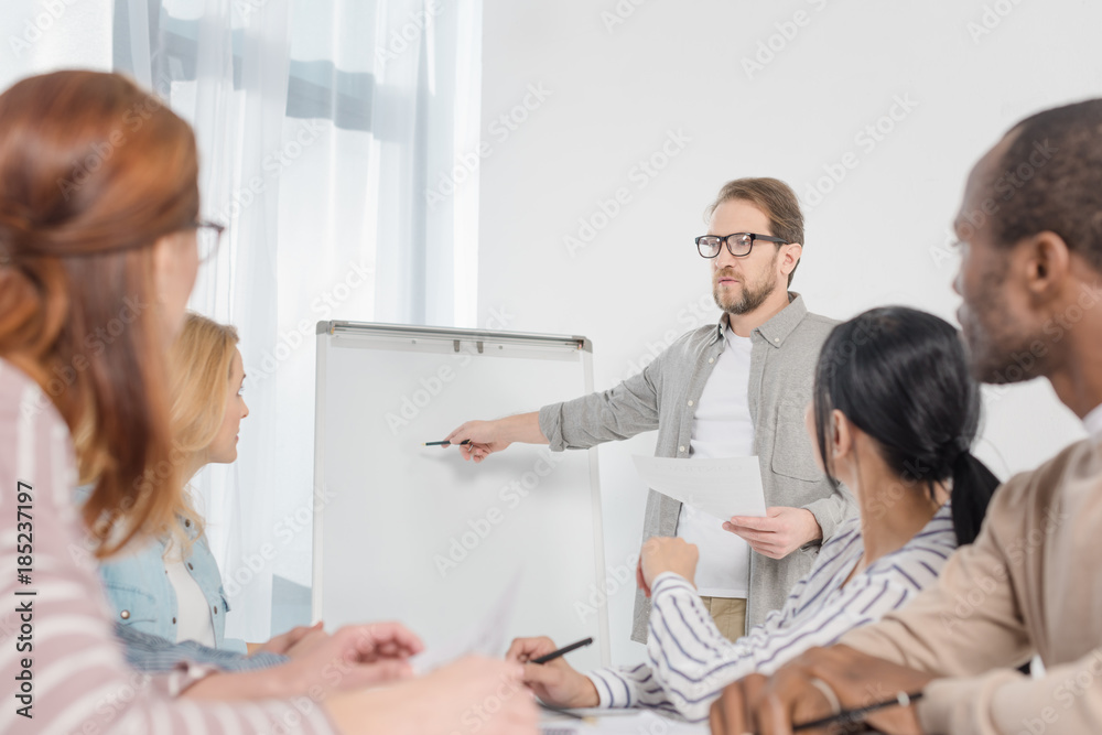 Fototapeta premium male psychoanalyst pointing at whiteboard white people gathered around table at anonymous group therapy
