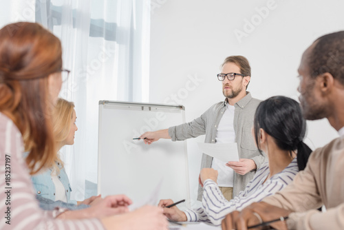 male psychoanalyst pointing at whiteboard white people gathered around table at anonymous group therapy