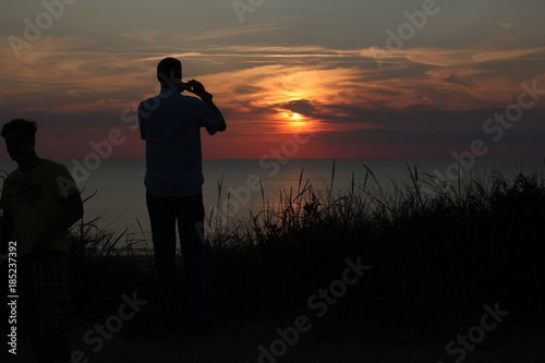 Sonnenuntergangsstimmung auf dem Roten Kliff in Richtung Nordsee mit Fotograf im Vordergrund und die Sonne zwischen Wolken im Hintergrund .Where: Wenningstedt, Sylt.When: 25.07.2014.