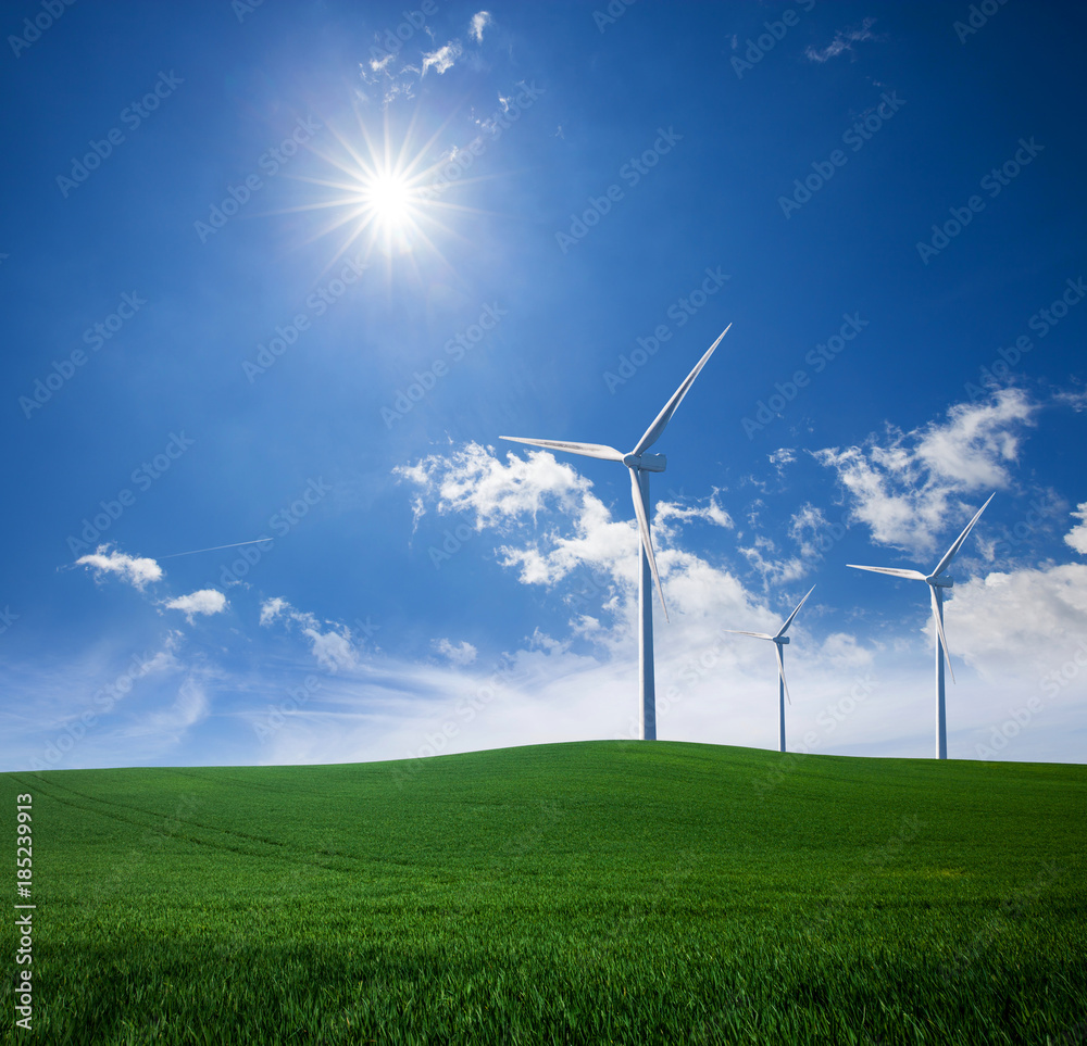 Wind power turbine station on green grass lawn over blue sunny sky Wind power turbine station on green grass lawn over blue sunny sky