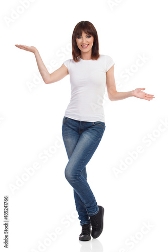 Beautiful Smiling Woman In Jeans And White T-Shirt Is Standing With Hands Raised And Presenting