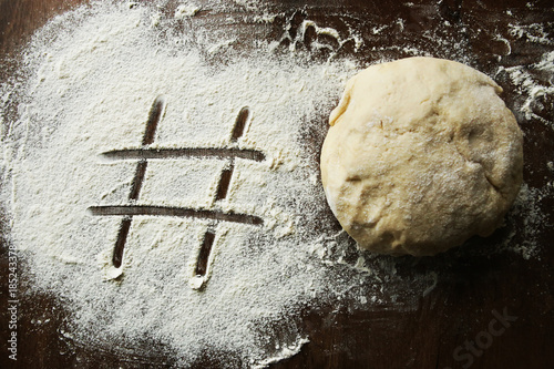 Hashtag written in flour and raw ball of dough. Number sign on floured wooden surface and fresh yeast dough for baking.
