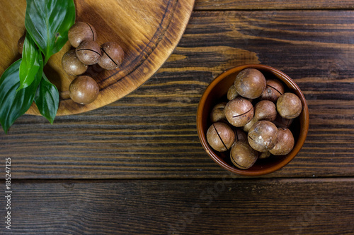 Top view of macadamia nuts in brown ceramic bowl on wooden table.