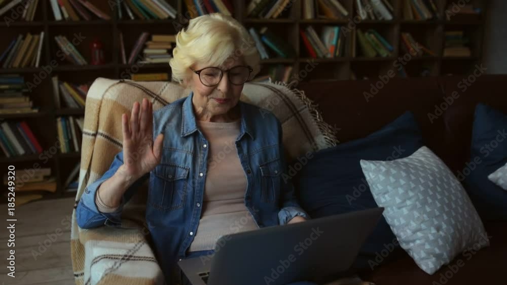Glad to see you. Cheerful elderly woman using her laptop and communicating through the Internet while resting at home