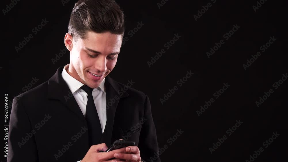 A smiling guy in a suit is typing something in his phone A smiling guy in a suit is typing something in his phone