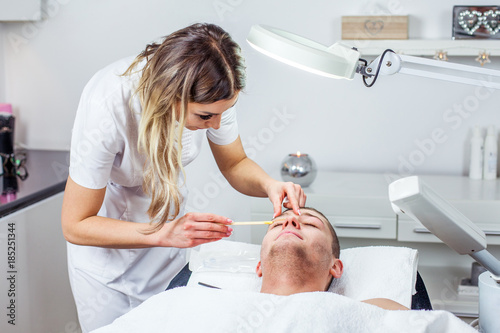 Cosmetologist woman is doing eyebrow modeling for man by wax for epilation. Cosmetological clinic. Healthcare