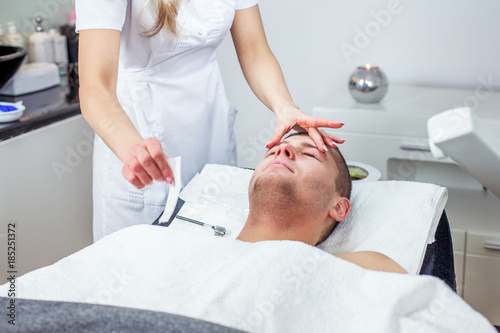 Cosmetologist woman is doing eyebrow modeling for man by wax for epilation. Cosmetological clinic. Healthcare