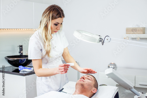 Cosmetologist woman is doing eyebrow modeling for man by wax for epilation. Cosmetological clinic. Healthcare
