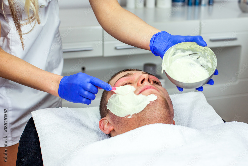 Cosmetologist is doing face mask for young boy / man. Model, close-up. Cosmetological clinic. Healthcare Cosmetologist is doing face mask for young boy / man. Model, close-up. Cosmetological clinic. Healthcare