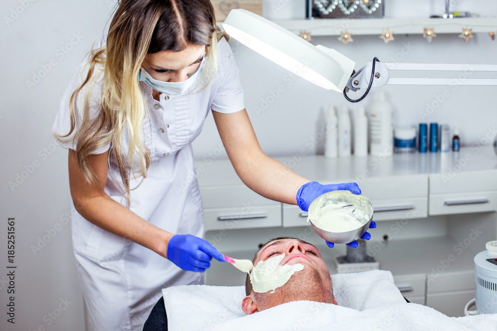Cosmetologist is doing face mask for young boy / man. Model, close-up. Cosmetological clinic. Healthcare Cosmetologist is doing face mask for young boy / man. Model, close-up. Cosmetological clinic. Healthcare