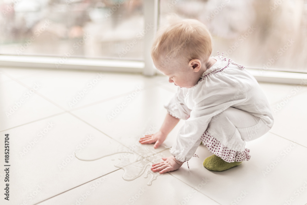 baby girl is touching by her hands a spilled water on the floor baby girl is touching by her hands a spilled water on the floor