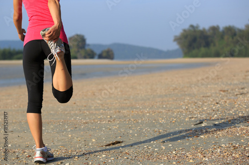 Young fitness woman warming up on sandy beach