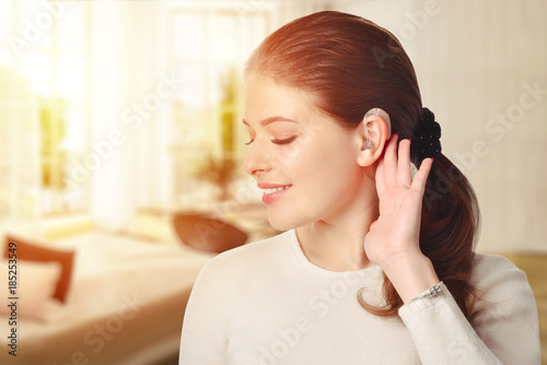 A girl with a hearing aid. The girl assumes hearing aid. In the room. Happy girl that hears well again