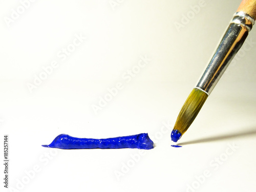 Brush with blue paint next to a strip of acrylic paint squeezed out of the tube.