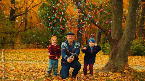 Grandfather is exploding party cracker in the autumn park with his grandsons