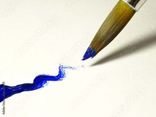 Synthetic brush with blue acrylic paint, which has just been drawn wavy line.