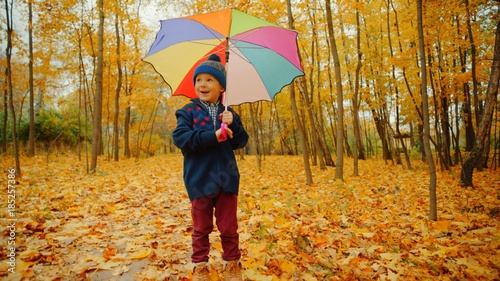 Little boy with umbrella is playing with fallen leaves