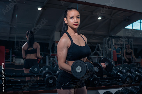 Muscular girl posing with dumbbells in the gym