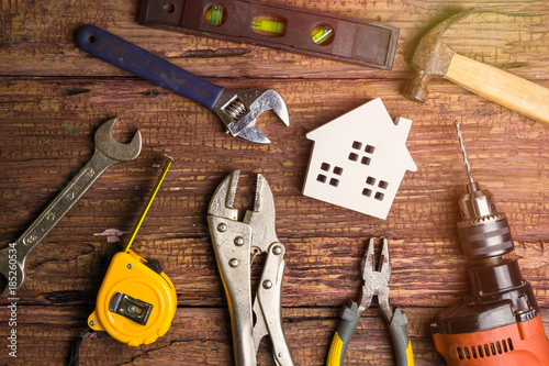 Wooden white house toy and construction tools on wooden background with copy space.Real estate concept, New house concept, Finance loan business concept, Repair maintenance concept.