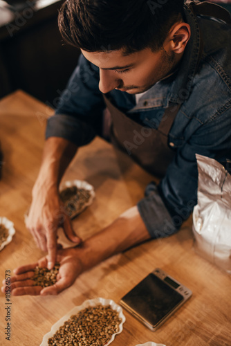 selective focus of man checking coffee beans quality at wooden table