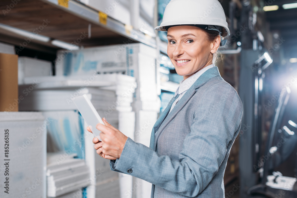 Fototapeta premium female inspector in helmet using digital tablet in warehouse