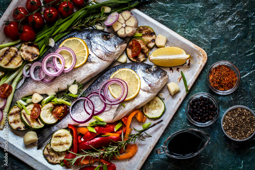 Dorada fish with vegetables, lemon, spices and greens on a blue background